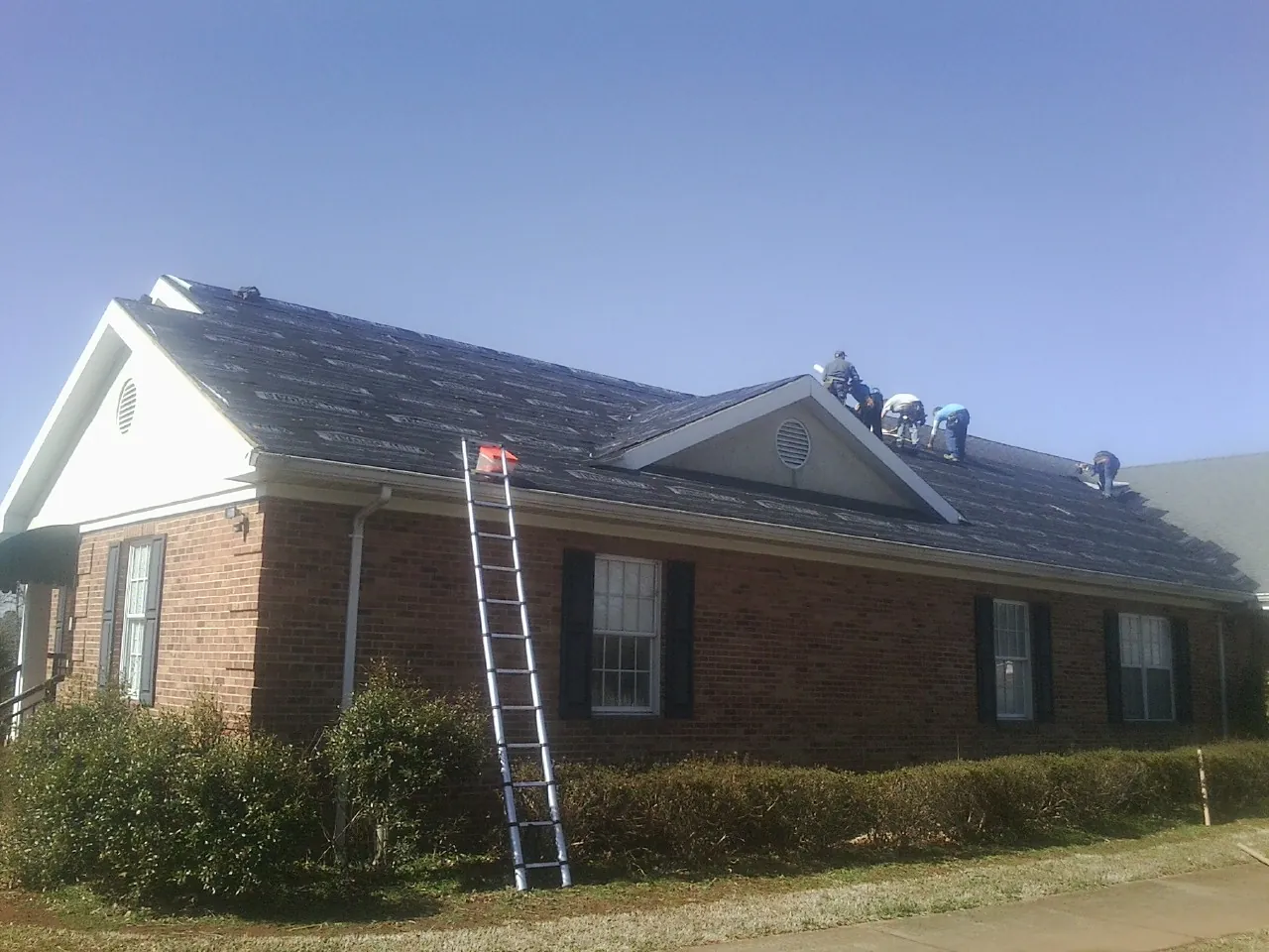 Crew tearing shingles off a brick ranch roof with a ladder set — Metal Roof Repair work by our crew in Quincy
