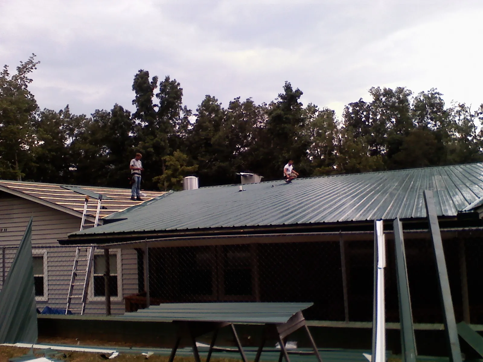 Two roofers installing green metal panels above a covered porch in Quincy